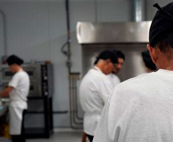Persona en formación como ayudante de cocina, aprendiendo técnicas culinarias en un entorno formativo adaptado